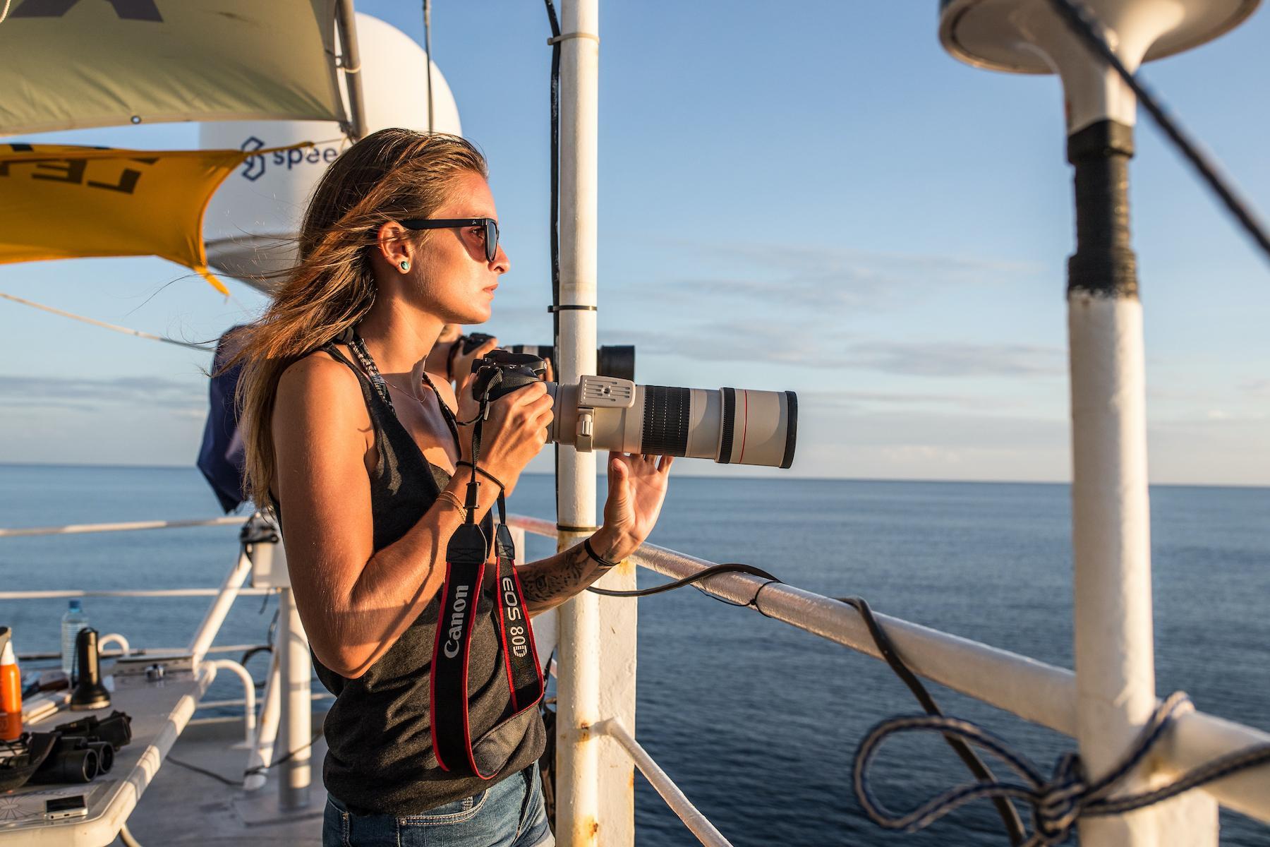 Margot, avec son appareil photo, sur un bateau, regardant l'horizon